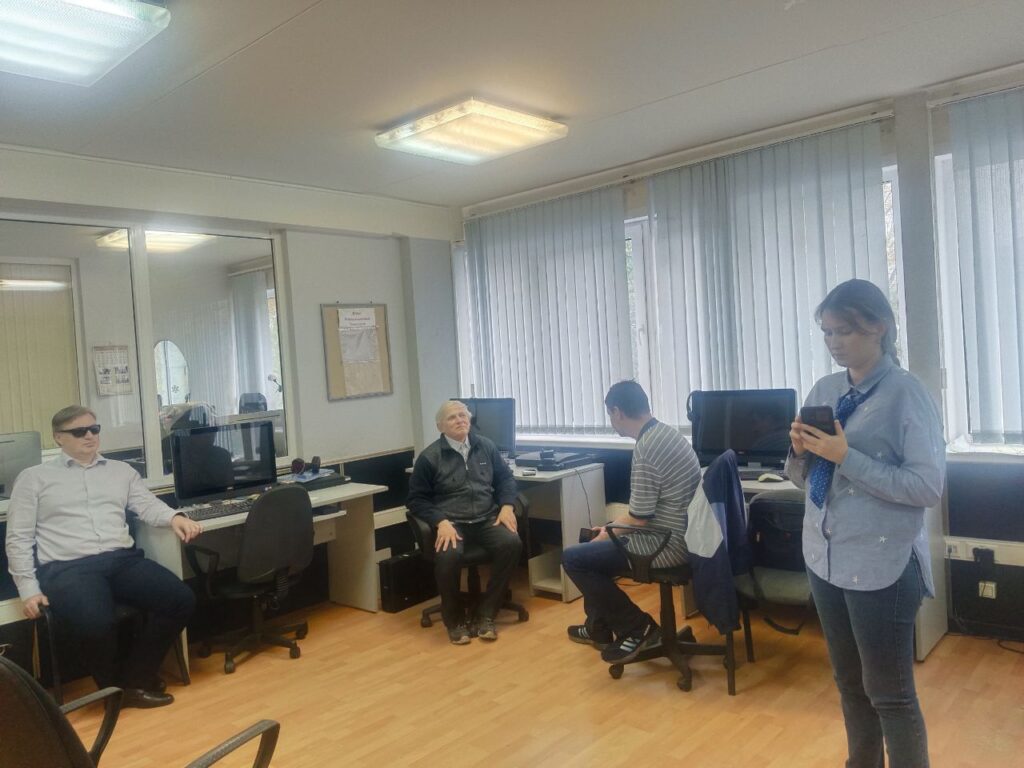 Проведение итоговой аттестации в компьютерном классе. Одна из слушательниц стоит в центре класса, в её руках смартфон.