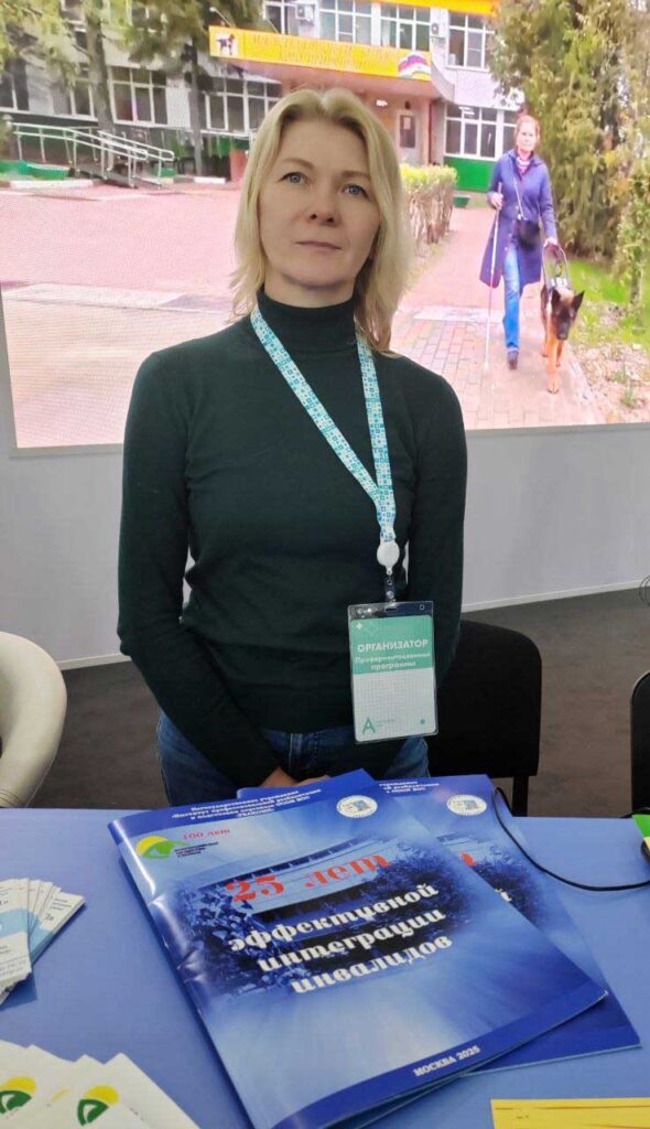 Тифлокомментарий ко второй фотографии: Старший психолог-реабилитолог Меланченко Л.Л. у стенда Всероссийского общества слепых. Перед ней на столе юбилейные издания Института «Реакомп».