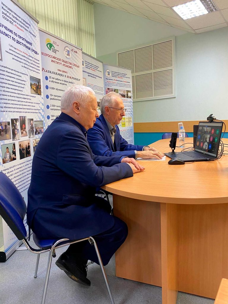 Тифлокомментарий: в конференц-зале Института «Реакомп» проходит дистанционное занятие с вновь избранными секретарями и председателями МО ВОС. Спикером выступает вице-президент ВОС А.И. Коняев, рядом с ним генеральный директор Института «Реакомп» С.Н. Ваньшин. Перед ними ноутбук с подключенными к видео-конференции слушателями.