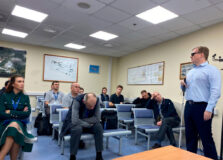 Тифлокомментарий: Е.Е. Арнапольский стоит вполоборота перед сотрудниками группы организации обслуживания маломобильных пассажиров аэропорта Внуково. На нём тёмные очки, в правой руке белая трость. Взгляды большинства сотрудников устремлены в его сторону.