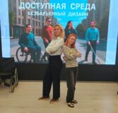 Начальник отдела реабилитации инвалидов Швырева Е.Н. и ведущий психолог-реабилитолог Макаренко А.С. в лектории. За ними большой экран с названием программы "Доступная среда. Безбарьерный дизайн. Слева от экрана - инвалидная коляска.