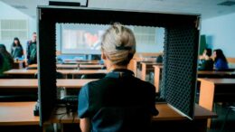 Тифлокомментарий к фотографии: в конференц-зале Института "Реакомп", спиной к нам, в кабине для тифлокомментирования расположился будущий тифлокомментатор. Перед ней – ряды парт, а на большом экране проецируется фильм. Идет обучение.