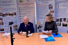 Тифлокомментарий к первому изображению. В аудитории перед камерой автор российской концепции тифлокомментирования С.Н. Ваньшин и его секретарь-референт Ю.О. Друцкая. В руках Сергея Николаевича листы бумаги с шрифтом Брайля, позади информационные стенды о деятельности Института